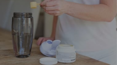 Person scooping powder into a shaker bottle on a kitchen counter.