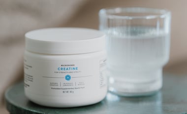 Creatine supplement container beside a glass of water with a spoon, showing powder dissolving.