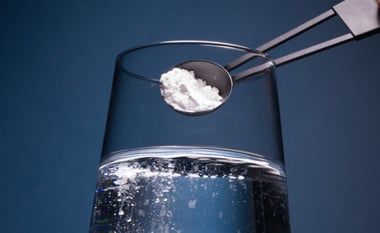 Scoop of creatine powder being added to a glass of water, with powder beginning to dissolve.