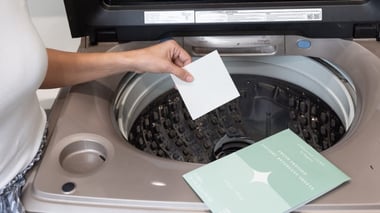 Hand placing a laundry sheet into an open top-loading washing machine.
