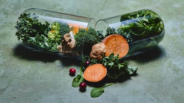 Open capsule filled with fresh vegetables like kale, spinach, broccoli, mushrooms, and sweet potato, symbolizing plant-based nutrition.