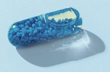 Close-up of a translucent capsule filled with small blue particles against a soft blue background.