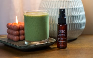 Green smoothie and wellness spray bottle placed on a table beside a book.