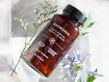 Harmonia supplement bottle displayed with flowers on a light background.