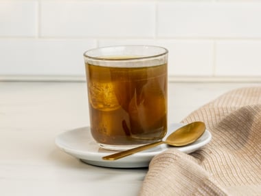 Glass of Ionix supreme on a saucer with a spoon and cloth napkin on a kitchen counter.