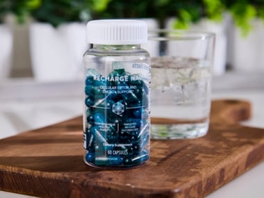 Recharge NAD supplement bottle next to a glass of water on a wooden surface.