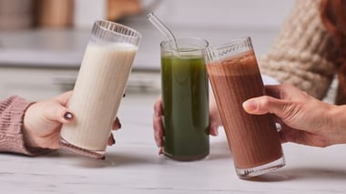 Three people holding glasses of shakes in different flavors—vanilla, green, and chocolate.