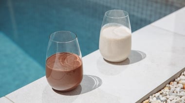 Two glasses of shakes, one chocolate and one vanilla, placed by a poolside.