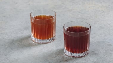 Two glasses of amber-colored tea placed on a light surface.