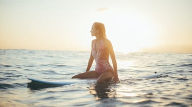 Woman sitting on a surfboard in the ocean at sunset.