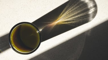 Top view of a dark herbal drink in a glass casting a long shadow on a light surface.