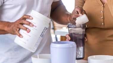 Two people preparing a shake by scooping powder into a blender bottle.