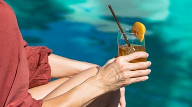 Person relaxing by water holding a refreshing drink with a citrus garnish.