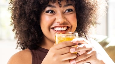 Smiling woman holding and enjoying a glass of golden-colored beverage.