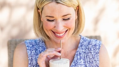 Smiling woman drinking a creamy shake through a straw.