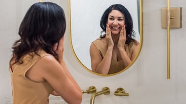 Woman in a bathroom washing her face.