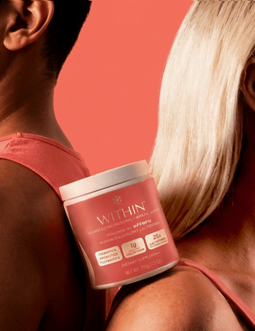 Two people standing back to back against a coral-colored background, with a container of ‘Within Advanced Microbiome + Immune Support’ positioned between their shoulders.
